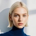 The sample image of a fashion model with a clean face light golden short hair a navy blue high neck sweater and a light colored background